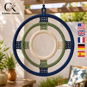 Op de afbeelding: Een cirkelvormige macramé wandhanger bestaande uit drie concentrische ringen verbonden door geweven dwarsbalken. De buitenste ring is donker marineblauw, de middelste ring is saliegroen en de binnenste ring is crèmekleurig.