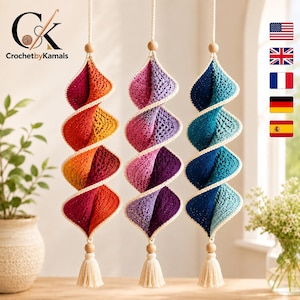 Pode incluir: Três ornamentos de crochê em espiral suspensos com um gradiente de cores. O ornamento da esquerda transita do vermelho para o laranja, o central do rosa para o roxo e o da direita do azul escuro para o azul claro, com bordas e borlas creme.