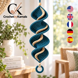 May include: A hanging crochet spiral decoration featuring deep teal and beige yarn. The structure consists of four interconnected teal diamond-shaped segments with a beige spiral accent running through the center, finished with wooden beads and a ring.