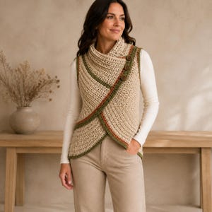 Op de afbeelding: Een mouwloos gehaakt vest in een lichtbeige kleur met een overslag aan de voorzijde en drie donkerbruine knopen. De randen zijn afgewerkt met een decoratieve bies in olijfgroen en roestoranje, gedragen over een wit shirt met lange mouwen en broek.