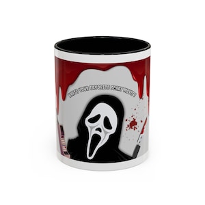 May include: A white ceramic mug with a black interior and rim, featuring a graphic of a masked figure in a black hooded robe. The design includes red blood drips, a vintage telephone, a knife, and the text "WHAT'S YOUR FAVORITE SCARY MOVIE?"