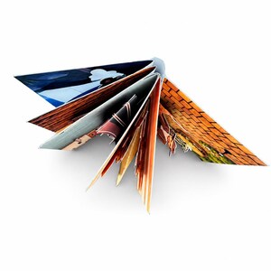 May include: A fan-folded book with multiple pages spread open, displaying various printed images including a blue sky, a brick wall, and abstract patterns in shades of orange, brown, and black, creating a star-like geometric shape.