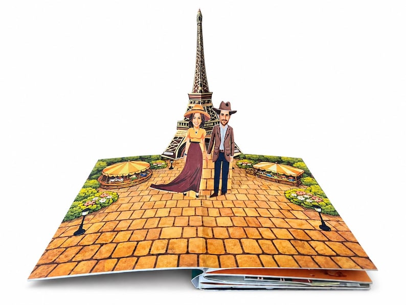 A personalized page from Our Adventure Book, a 3D pop-up book featuring a hand-illustrated Eiffel Tower. Two custom illustrated figures, created from the customer's own photos, stand together on a cobblestone path surrounded by green gardens and striped market stalls.