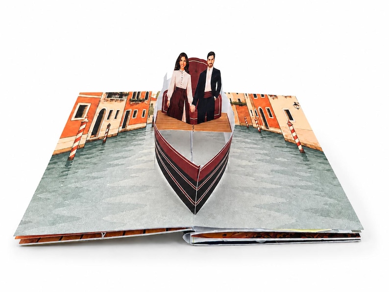 May include: A pop-up book featuring a three-dimensional paper gondola on a canal. Inside the boat, two figures stand holding hands. The background displays illustrated buildings along a waterway with red and white striped mooring poles.