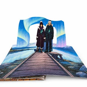 May include: A pop-up book spread featuring a three-dimensional illustration of two figures standing on a wooden pier. The background displays a vibrant blue and purple aurora borealis over a lake. The figures wear dark winter coats and hats.