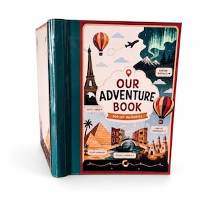 May include: A hardcover book titled Our Adventure Book Pop-Up Memories with a dark teal spine. The cover features illustrations of the Eiffel Tower, hot air balloons, the Aurora Borealis, Egyptian pyramids, and a Venice gondola.
