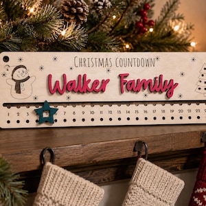 Pu&ograve; includere: Un cartello rettangolare in legno per il conto alla rovescia di Natale con la scritta "CHRISTMAS COUNTDOWN" e "Walker Family" in rilievo rosso. Include un pupazzo di neve inciso al laser, un albero di Natale, fiocchi e una stella turchese.