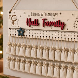 Pu&ograve; includere: Un cartello per il conto alla rovescia di Natale in legno chiaro con la scritta "CHRISTMAS COUNTDOWN" e "Hall Family" in rosso. Include un segnaposto a forma di stella blu scuro scorrevole, i numeri da 1 a 24 e ventiquattro sacchetti in tessuto beige.