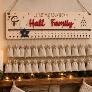 Pu&ograve; includere: Un cartello rettangolare in legno per il conto alla rovescia di Natale con il testo "CHRISTMAS COUNTDOWN" e "Hall Family" in rosso. Presenta un pupazzo di neve, un albero, i numeri da 1 a 24 e una stella blu. Ventiquattro sacchetti di tela beige pendono.