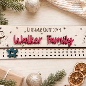 Pu&ograve; includere: Un cartello rettangolare in legno per il conto alla rovescia di Natale con il testo "CHRISTMAS COUNTDOWN" e "Walker Family" in lettere rosse in rilievo. Include un pupazzo di neve, un albero di Natale e una stella scorrevole color ottanio.