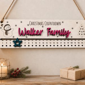 Pu&ograve; includere: Un cartello rettangolare in legno per il conto alla rovescia di Natale con corda di iuta. Il cartello presenta la scritta "CHRISTMAS COUNTDOWN" e "Walker Family" in rosa, con un pupazzo di neve, un albero di Natale e una stella blu per segnare i numeri da 1 a 24.