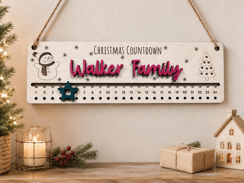 Pu&ograve; includere: Un cartello rettangolare in legno per il conto alla rovescia di Natale con corda di iuta. Il cartello presenta la scritta "CHRISTMAS COUNTDOWN" e "Walker Family" in rosa, con un pupazzo di neve, un albero di Natale e una stella blu per segnare i numeri da 1 a 24.