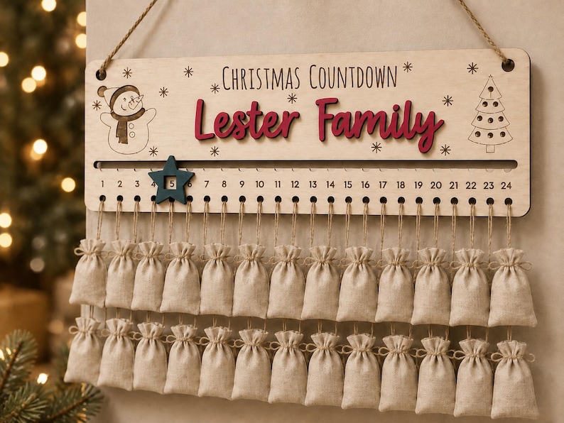 Pu&ograve; includere: Un cartello in legno per il conto alla rovescia di Natale con la scritta "Christmas Countdown" e "Lester Family" in rosso. Presenta un pupazzo di neve, un albero di Natale e i numeri da 1 a 24 con un segnaposto a stella blu. Ventiquattro sacchetti in tessuto beige pendono sotto.