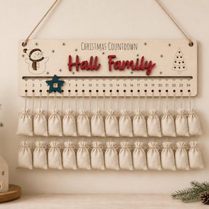 Pu&ograve; includere: Un cartello per il conto alla rovescia di Natale in legno chiaro con il testo "Christmas Countdown" e "Hall Family" in rosso. Presenta un'illustrazione di un pupazzo di neve e un albero, una traccia numerata da 1 a 24 con un segnaposto a stella blu scuro e due file di piccoli sacchetti in tessuto beige.