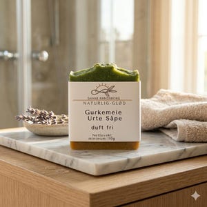 Puede incluir: Una pastilla de jabón de hierbas rectangular con una etiqueta de papel blanco que presenta el texto SHANE RANDSBORG NATURLIG-GLØD, Gurkemeie Urte Såpe, duft fri y Nettovekt: minimum 110g. El jabón tiene una parte superior verde texturizada y una base ámbar.