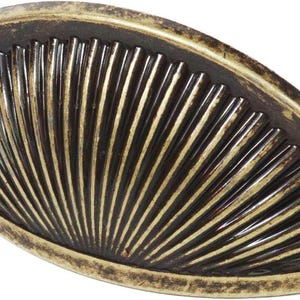 May include: A semi-circular metal drawer pull with a distressed antique brass finish. The surface features a radiating fan pattern of vertical ridges that extend from the centre to the curved outer edge, creating a textured, shell-like appearance.