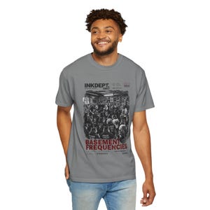 Może przedstawiać: Szary t-shirt z krótkim rękawem z nadrukiem graficznym przedstawiającym zespół występujący w piwnicy. Tekst zawiera napisy INKDEPT, BASEMENT FREQUENCIES oraz inne drobne szczegóły. Projekt jest czarno-biały z czerwonymi akcentami w tytule.