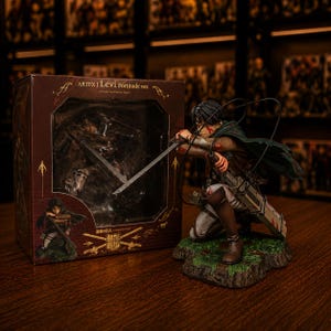 Könnte beinhalten: Eine ARTFX J Levi Fortitude ver. Figur aus Attack on Titan, die einen Charakter mit dunkelgrünem Umhang und braunen Stiefeln zeigt, der auf einer strukturierten Basis kniet und ein silbernes Schwert hält. Die Verpackung zeigt das Motiv.