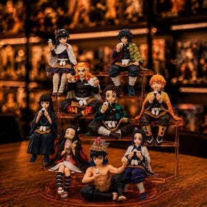 Könnte beinhalten: Eine Sammlung von neun Anime-Charakterfiguren, die auf einem abgestuften Ständer angeordnet sind. Jede Figur trägt ein individuelles Outfit mit gemusterten Haoris, dunklen Uniformen und Accessoires, wobei einige kleine weiße Speisen halten.