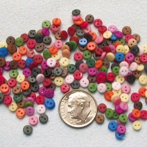 May include: A large assortment of colorful plastic buttons in various shades of red, blue, green, yellow, pink, brown, and white. The buttons are two-holed and are scattered on a white surface.