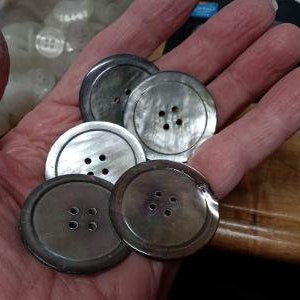 May include: Five round, black and white, mother-of-pearl buttons with four or five holes each.