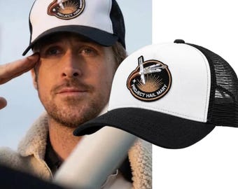 May include: A white and black trucker hat featuring a circular embroidered patch on the front. The patch displays a stylised sun, a rocket, and the text Project Hail Mary. The hat has a solid white front panel and a black mesh back.
