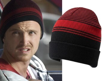 May include: A knitted beanie hat featuring a cuffed design with a colour-blocked pattern. The lower portion is solid black, whilst the upper section displays alternating horizontal stripes in vibrant red and black, creating a distinct two-tone appearance.