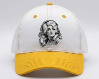 May include: A white baseball cap with a mustard yellow brim and a button on top. The front panel features a centred, black and white graphic illustration of a person with voluminous, wavy hair and hoop earrings, wearing a collared shirt.