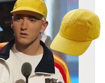 May include: A bright yellow five-panel cap featuring a structured crown, a flat brim, and small ventilation eyelets on the side panels. The hat is constructed from a solid-coloured fabric with visible stitching along the seams and brim.