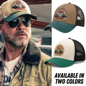 May include: Two trucker hats featuring a circular patch with an airplane, mountains, and the text "NORTHERN SKIES BUSH PILOT". One hat has a tan front and dark green brim with black mesh, while the other has an off-white front and green brim.