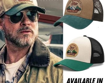 May include: Two trucker hats featuring a circular patch with an aeroplane, mountains, and the text "NORTHERN SKIES BUSH PILOT". One hat has a tan front and dark green brim with black mesh, while the other has an off-white front and green brim.