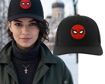 May include: A black baseball cap featuring a circular red patch on the front panel. The patch displays a black spiderweb pattern and two white eye shapes. The cap has a structured crown, a curved brim, and red detailing on the underside of the brim.