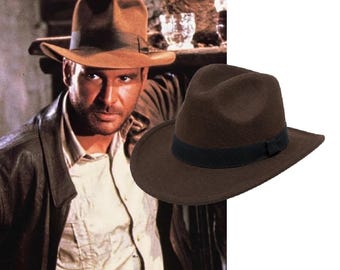 May include: A dark brown felt fedora hat featuring a structured crown with a centre crease and a wide brim. The hat is accented with a solid black grosgrain ribbon band encircling the base of the crown, providing a distinct contrast to the dark brown felt.