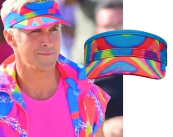 May include: A visor featuring a vibrant, multi-coloured abstract pattern in shades of bright blue, hot pink, yellow, and orange. The visor has a curved brim and a structured band, showcasing a bold, psychedelic-inspired design throughout the fabric.
