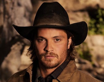 May include: A black felt cowboy hat with a structured crown and a wide, curved brim. The hat features a dark, narrow band around the base of the crown, providing a clean, classic silhouette that sits atop the head with a slight downward tilt.