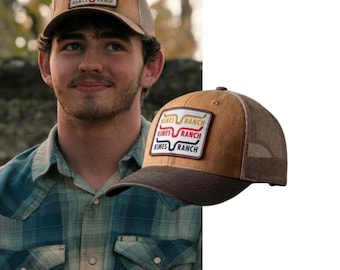 May include: A tan and brown trucker hat featuring a rectangular patch on the front. The patch displays the text KIMES RANCH in black, red, and yellow, accompanied by a stylised longhorn steer logo. The hat has a mesh back and a solid brim.