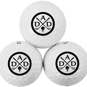 May include: Three white golf balls with a black logo featuring the letters "A D D" with crossed golf clubs and a golf ball in the center.