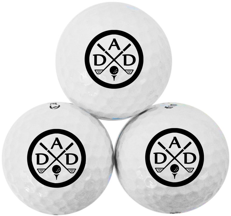 May include: Three white golf balls with a black logo featuring the letters "A D D" with crossed golf clubs and a golf ball in the center.