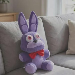 Peut inclure: Une peluche lapin violette avec de longues oreilles dressées, de grands yeux blancs à pupilles roses, un petit nez noir et un nœud papillon rouge vif. Le personnage présente une tête arrondie, un museau violet clair et un tissu doux.