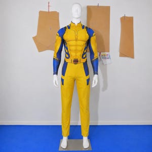 Puede incluir: Un mono de cuerpo entero amarillo y azul sobre un maniquí blanco. El traje presenta una pieza pectoral moldeada con músculos abdominales definidos, mangas largas y un cinturón con una hebilla rectangular roja y negra en la cintura.