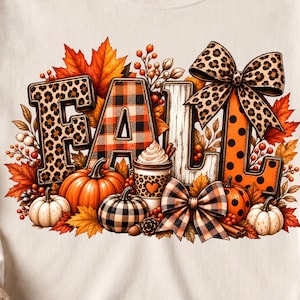 Puede incluir: Una camiseta de manga larga color crema con un estampado gráfico de la palabra FALL. Las letras están decoradas con patrones de leopardo, cuadros y lunares, rodeadas de hojas de arce naranjas, calabazas y una taza de café.
