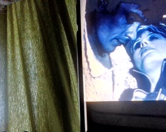 May include: A rectangular screen displaying a blue-toned film scene featuring two people in close proximity. The text on the screen reads Starring Marianne Faithfull and Alain Delon, Directed by Jack Cardiff. The screen is positioned next to green curtains.