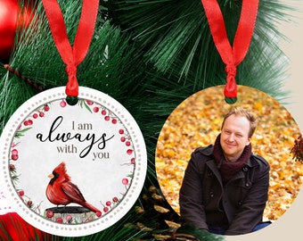 Könnte beinhalten: Zwei runde Weihnachtskugeln. Eine Kugel zeigt einen roten Kardinal mit dem Text "Ich bin immer bei dir". Die andere Kugel zeigt ein Foto einer lächelnden Person in einer Waldlandschaft.