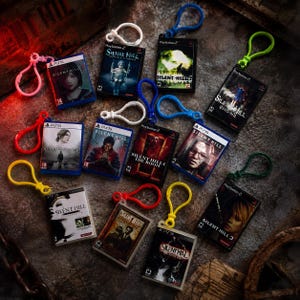 Puede incluir: Una colección de llaveros en miniatura con forma de cajas de videojuegos de Silent Hill que representan varios títulos de la serie. Cada pequeña caja rectangular de plástico muestra la carátula auténtica y la marca de la consola.