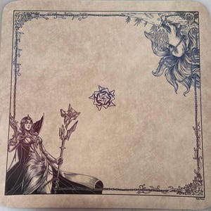 May include: A square beige playmat featuring a dark brown line art illustration. The design includes a figure holding a staff, a multi-tailed creature in the corner, a central star-like emblem, and a floral vine border with chains.