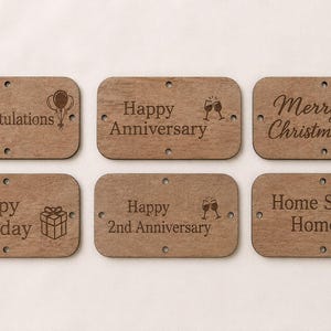 May include: Six rectangular brown wooden tags with rounded corners and four small holes each. The tags feature laser-engraved text and icons: Congratulations with balloons, Happy Anniversary with glasses, Merry Christmas with Santa, Happy Birthday with a gift, Happy 2nd Anniversary with glasses, and Home Sweet Home with a house.