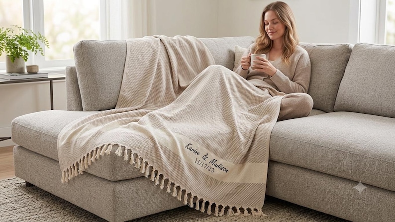 May include: A beige waffle-knit throw blanket with fringe trim on the edges. The blanket features dark embroidery with the text Karine & Madison and the date 11/17/23. The fabric has a textured grid pattern throughout the entire surface area.