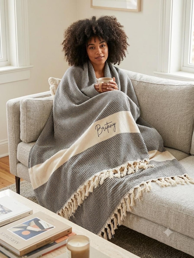 May include: A black and white woven throw blanket featuring a textured pattern, a wide cream-colored horizontal stripe across the center, and decorative fringe along the bottom edge. The name Britany is embroidered in black script on the stripe.