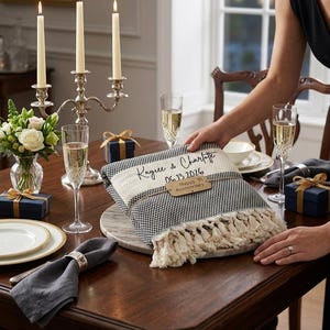 May include: A folded black and white woven throw blanket with fringe edges, personalized with the text Kaycee & Charlotte and the date 06.13.2026, featuring a wooden tag tied around the center that reads Happy Anniversary.