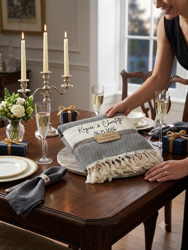 May include: A folded black and white woven throw blanket with fringe edges, personalized with the text Kaycee & Charlotte and the date 06.13.2026, featuring a wooden tag tied around the center that reads Happy Anniversary.
